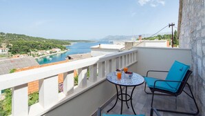 A balcony with a table and chair, overlooking a coastal view with buildings and greenery. - 3 bedroom cozy home in Povlja (Povlja)