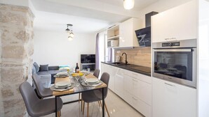 A modern kitchen with white cabinets, a built-in oven, and a dining area with a table set for four. - 3 bedroom cozy home in Povlja (Povlja)