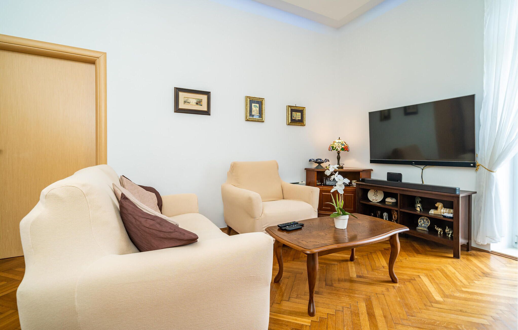 Una sala de estar con dos sofás color beige, una mesa de centro de madera, un televisor y un mueble con adornos.