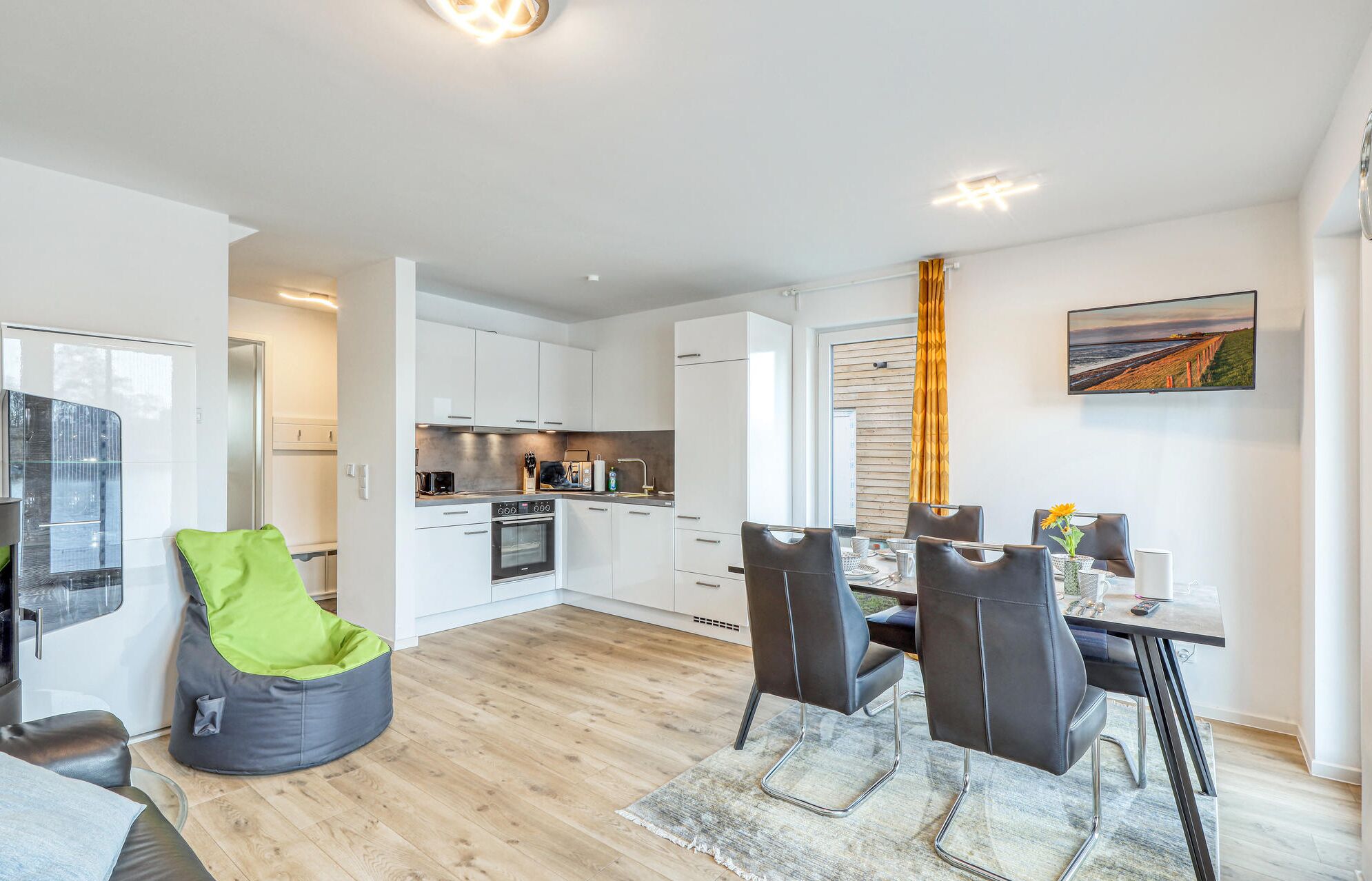 A modern apartment with a dining area, kitchen, and a large window.