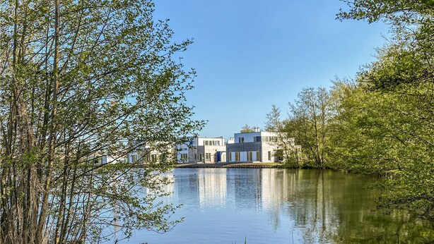 Un edifici modern amb una zona d'aigua que reflecteix la imatge, envoltat d'arbres.