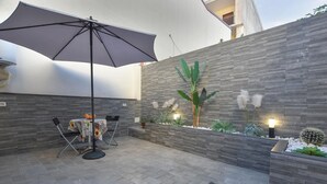 A patio area with a table and chairs, a large umbrella, and a decorative wall with plants and lighting. - Awesome home in Catania with sauna (Catania)