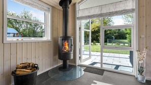 A room with a wood-burning stove, a window with a view of greenery, and a door leading outside. - Nice home in Tarm with sauna (Tarm)