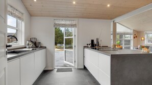 A modern kitchen with white cabinetry, a large island, and a view of the outdoors through a glass door. - Nice home in Tarm with sauna (Tarm)