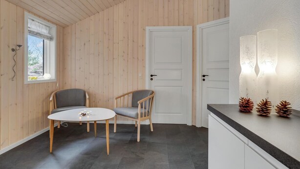 Une pièce aux murs en bois, une table ronde avec deux chaises, une porte blanche et un comptoir de cuisine décoré de pommes de pin.