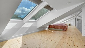 Une chambre mansardée avec de hauts plafonds, des fenêtres de toit, un plancher en bois et un lit.