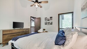 Une chambre à coucher comprenant un lit, une commode en bois, un téléviseur et un ventilateur de plafond.