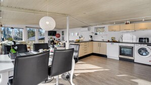 A modern kitchen with white cabinetry, a dining area with black chairs, and a large window overlooking a deck. - Stunning home in Roslev with kitchen (Roslev)