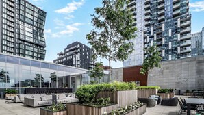 Un espace extérieur aménagé avec des meubles modernes, entouré de verdure et avec de grands bâtiments en arrière-plan.