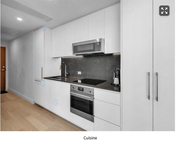 A modern kitchen with white cabinets, a microwave, a stove, and a sink.