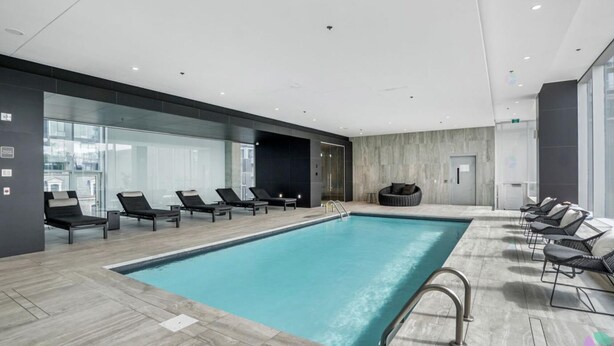 Une piscine intérieure moderne, dotée de chaises longues et d’un mur en verre.