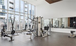 A modern gym with various exercise equipment, large windows, and a mirrored wall.