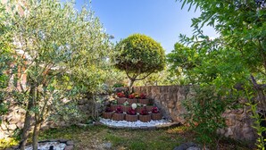 Un jardín con pared de piedra, un árbol y macizos de flores.