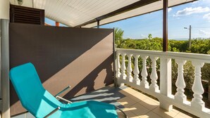 Un balcón con una silla azul, barandilla blanca y vistas a zonas verdes.
