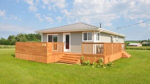 A single-story house with a front porch, a garage, and a small deck. - Renovated family cottage; walk to amazing beach, short drive to golf & town (Sea View)