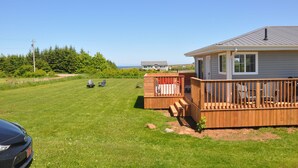 A residential property with a deck, a lawn, and a house in the background. - Renovated family cottage; walk to amazing beach, short drive to golf & town (Sea View)