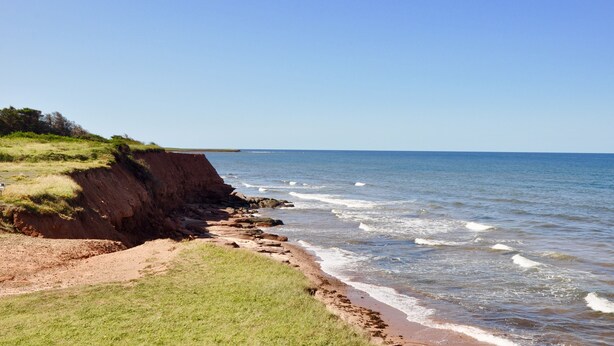 A coastal landscape with a sandy beach, grassy areas, and a cliff. - Renovated family cottage; walk to amazing beach, short drive to golf & town (Sea View)