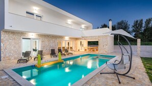 Ein modernes Haus mit Swimmingpool, Steinmauern und Sitzgelegenheiten im Freien.