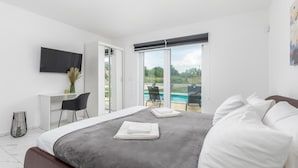 Ein modernes Hotelzimmer mit Bett, Schreibtisch, Stuhl, Fernseher und Blick auf einen Swimmingpool.