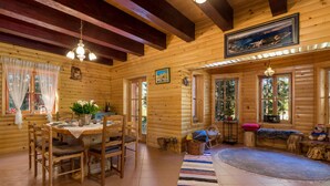 Ein gemütliches Blockhäuschen-Interieur mit Essbereich, einer Bank und einem großen Fenster mit Blick auf den Wald.