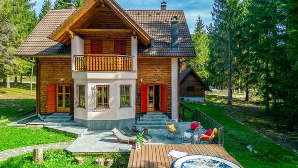 Eine zweistöckige Blockhütte mit Balkon, Whirlpool und Sitzgelegenheit im Freien.