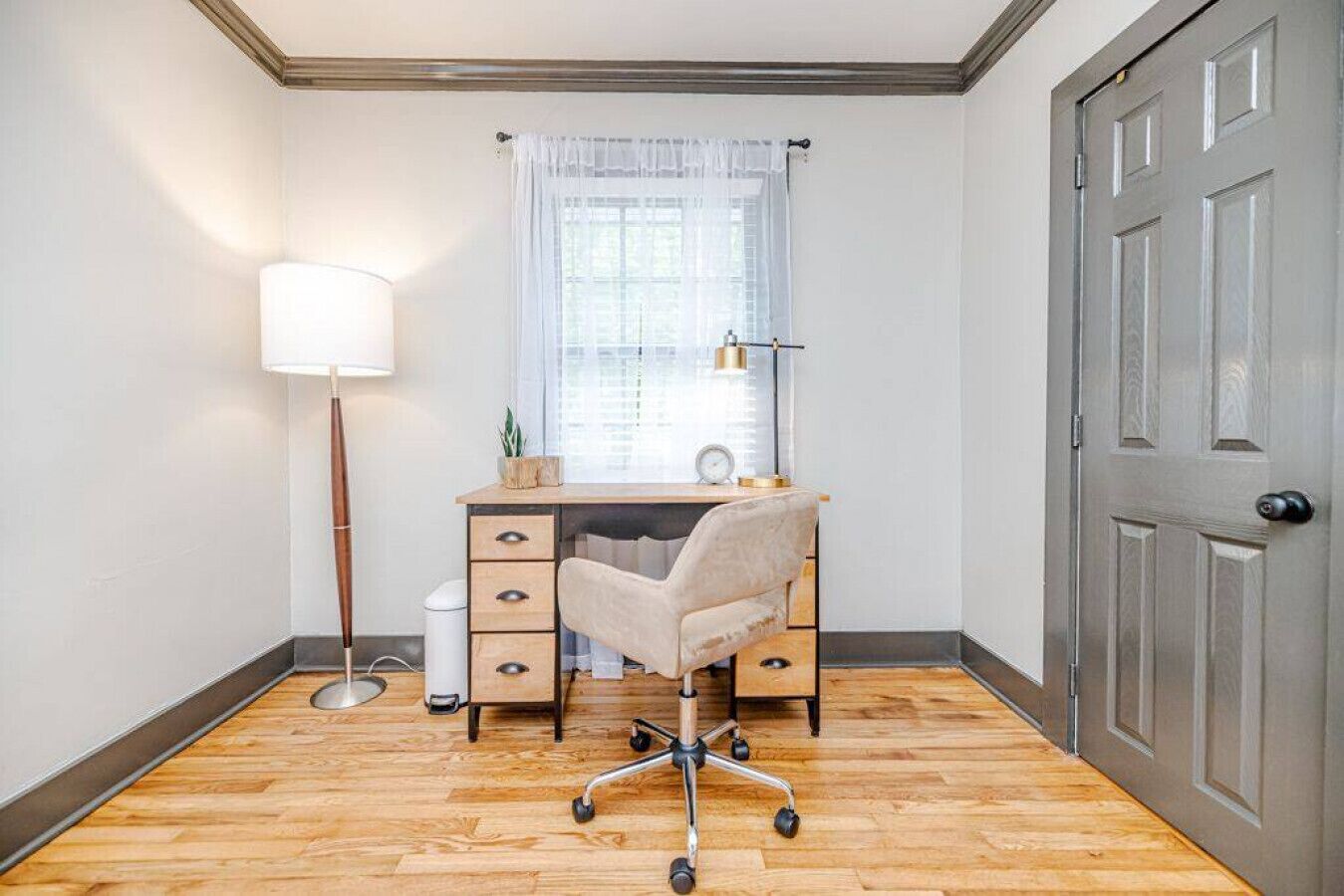 Quarto de canto com escrivaninha, cadeira, abajur e porta.