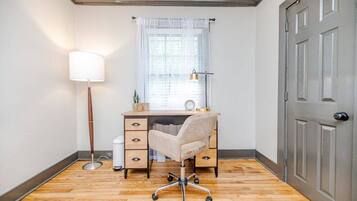 Quarto de canto com escrivaninha, cadeira, abajur e porta.