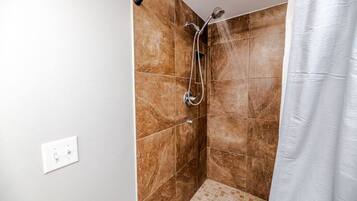 A shower with a handheld showerhead and a wall-mounted faucet, tiled walls, and a white curtain.