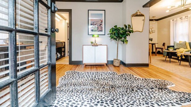 Un saló modern amb sòl de fusta, un camí de taula amb estampat de leopard, una taula de consola blanca amb una làmpada i una planta gran.