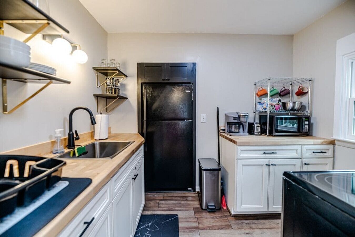 Una cocina compacta con un refrigerador negro, un lavamanos, una cafetera y un microondas.