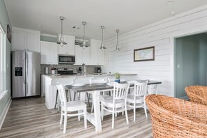 A modern kitchen with white cabinetry, stainless steel appliances, a central island with seating, and hanging pendant lights.