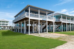 A two-story beachfront building with a balcony, a sign reading "Sunny 76", and a staircase leading to the upper level.