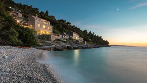 A coastal property with stone buildings, a pebble beach, and a calm sea.