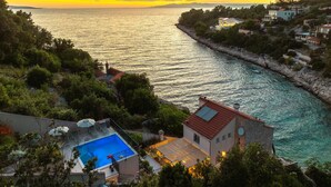 A coastal property with a swimming pool, a stone building, and a view of the sea.