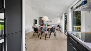 A modern kitchen with a large island, a dining area with a wooden table and chairs, and a view of the outdoors through large windows.