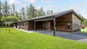 A modern building with a covered patio area, a wooden exterior, and a gravel driveway.