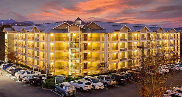 Stunning hotel with a central staircase connecting floors, surrounded by trees and a mountain range.