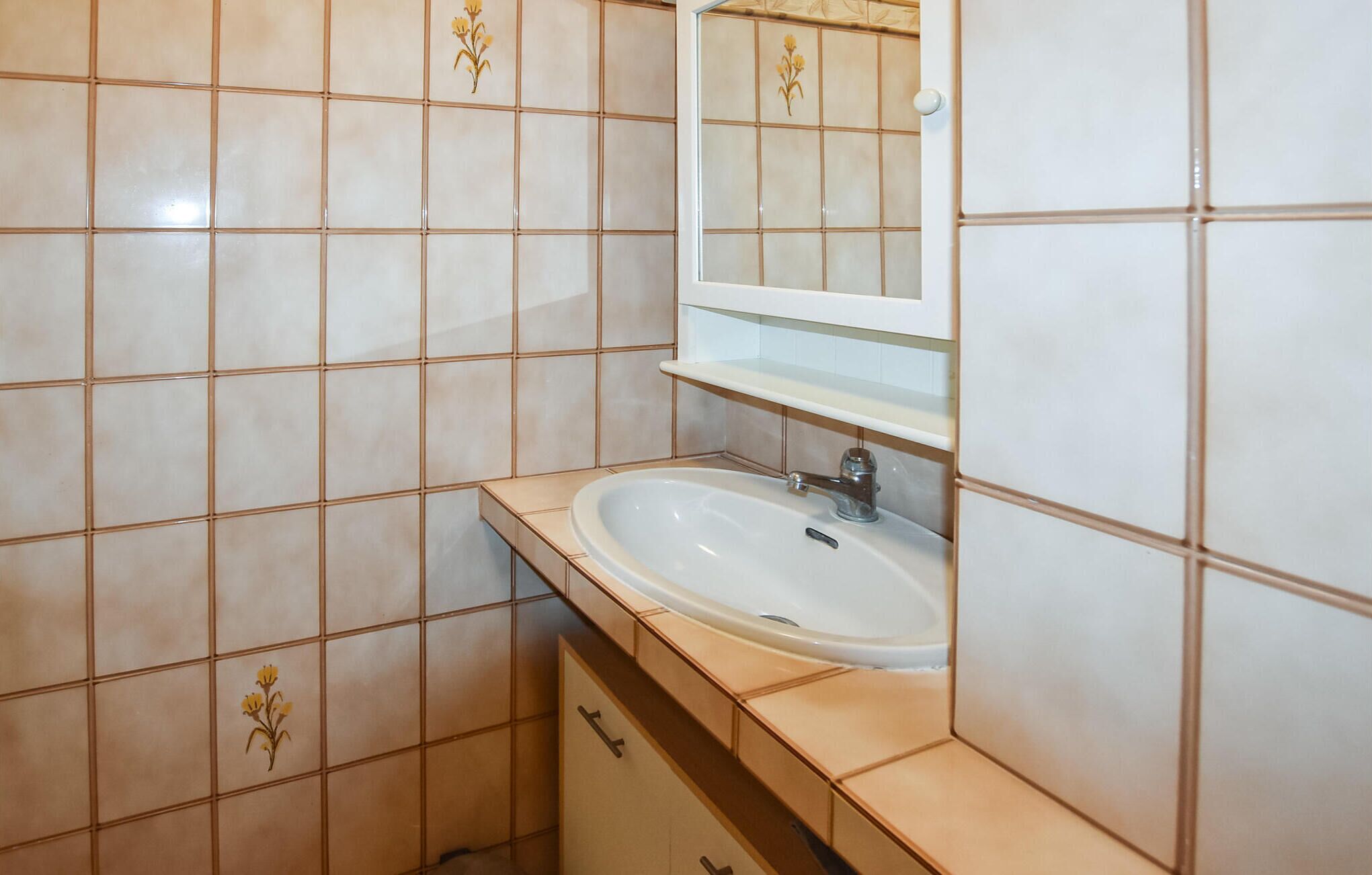 Un baño con un lavamanos blanco, un espejo encima y baldosas decorativas con motivos florales en las paredes.