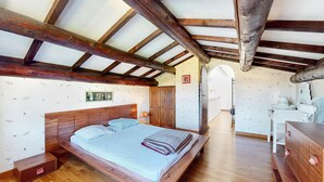 Ein Schlafzimmer mit einem Holzbett, einem Nachttisch, einer Kommode und einer Holzbalkendecke.