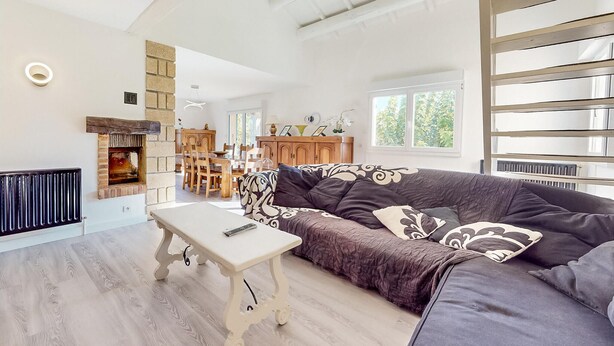 Ein geräumiges Wohnzimmer mit Kamin, einer Couch, einem Essbereich und Blick ins Freie.