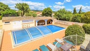 Ein Schwimmbad mit Glasveranda, Sitzgelegenheiten im Freien und einer überdachten Terrasse.