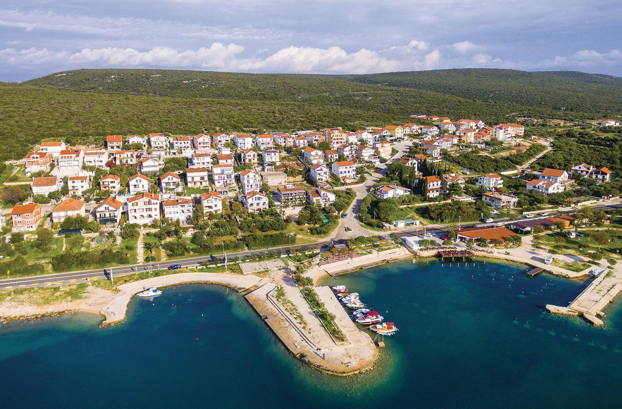 Vista aérea de una zona residencial costera con casas, un puerto deportivo y una carretera.