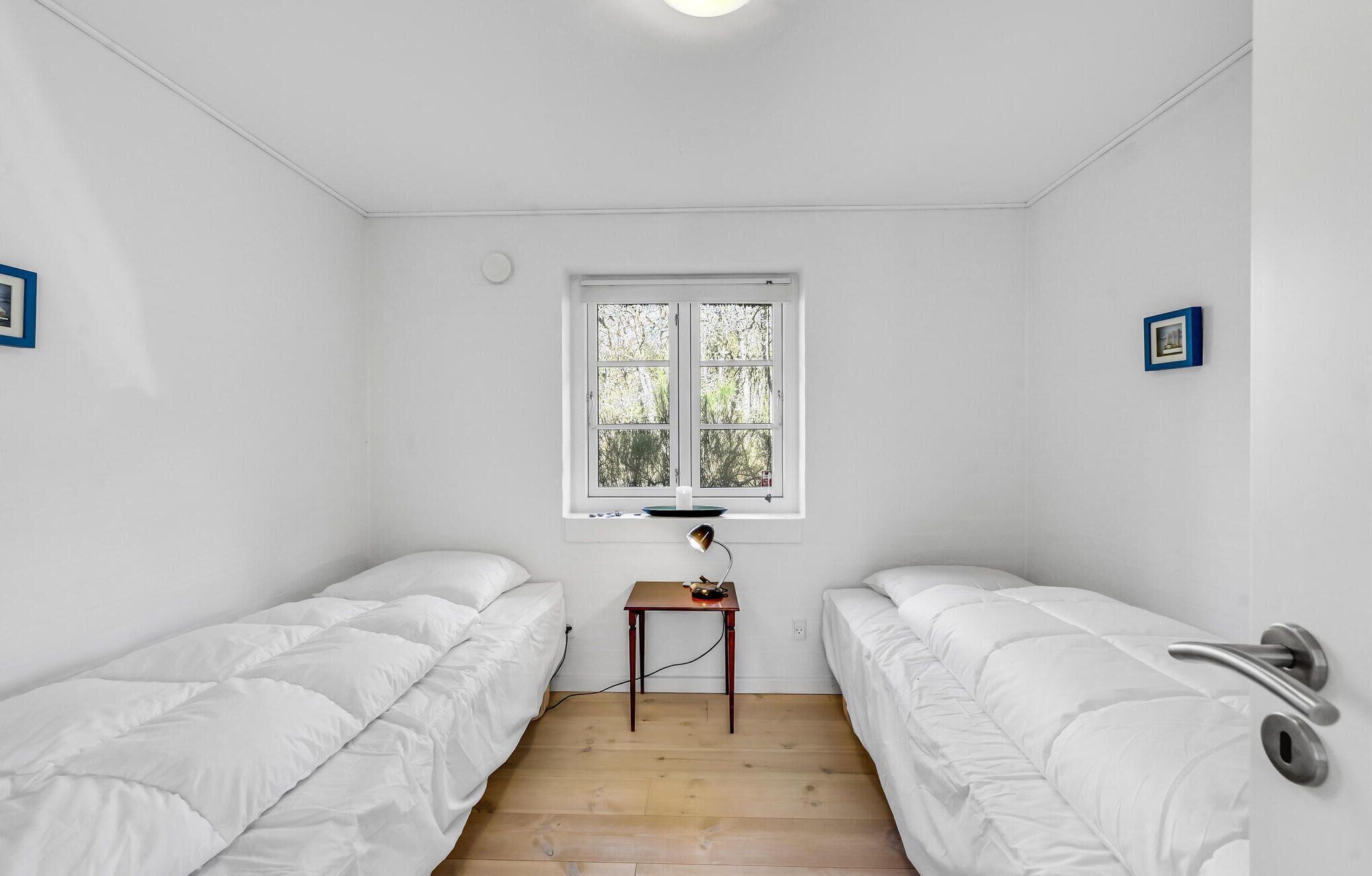 Une petite chambre propre, avec deux lits simples, une petite table et une fenêtre donnant sur les arbres.