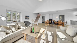 A spacious living area with a sofa, a coffee table, and a dining table. There is a staircase leading to another level.