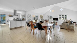 A spacious living area with a high ceiling, a dining table with chairs, a sofa, and a TV.