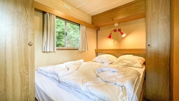 A bedroom with a bed, a window with curtains, and a wall-mounted lamp. - Gorgeous (sta)caravan in Tzummarum (Tzummarum)