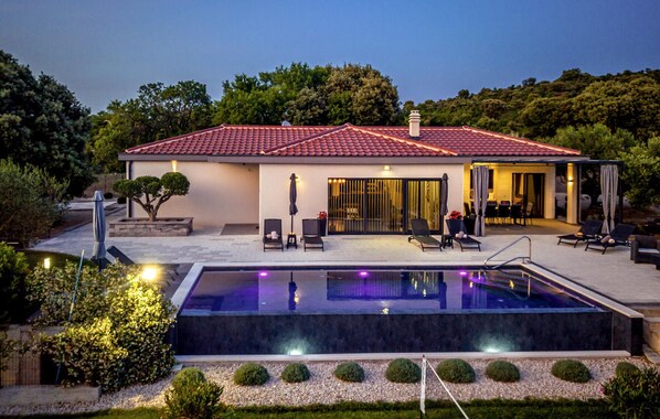 Une maison moderne dotée d’une piscine, d’un espace salon extérieur et d’un patio couvert.