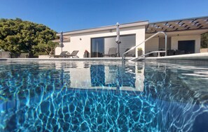 A clear swimming pool with a modern building in the background, including a covered patio area. - Amazing home in Polaca with private swimming pool, can be inside or outside (Polaca)