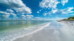 A beach with clear turquoise water, a sandy shore, and a partly cloudy sky.