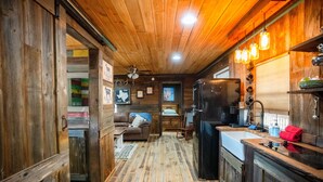 Een rustiek blokhutinterieur met houten wanden, een keuken, een woonkamer met bank en open haard, en een hal met vloerkleed.